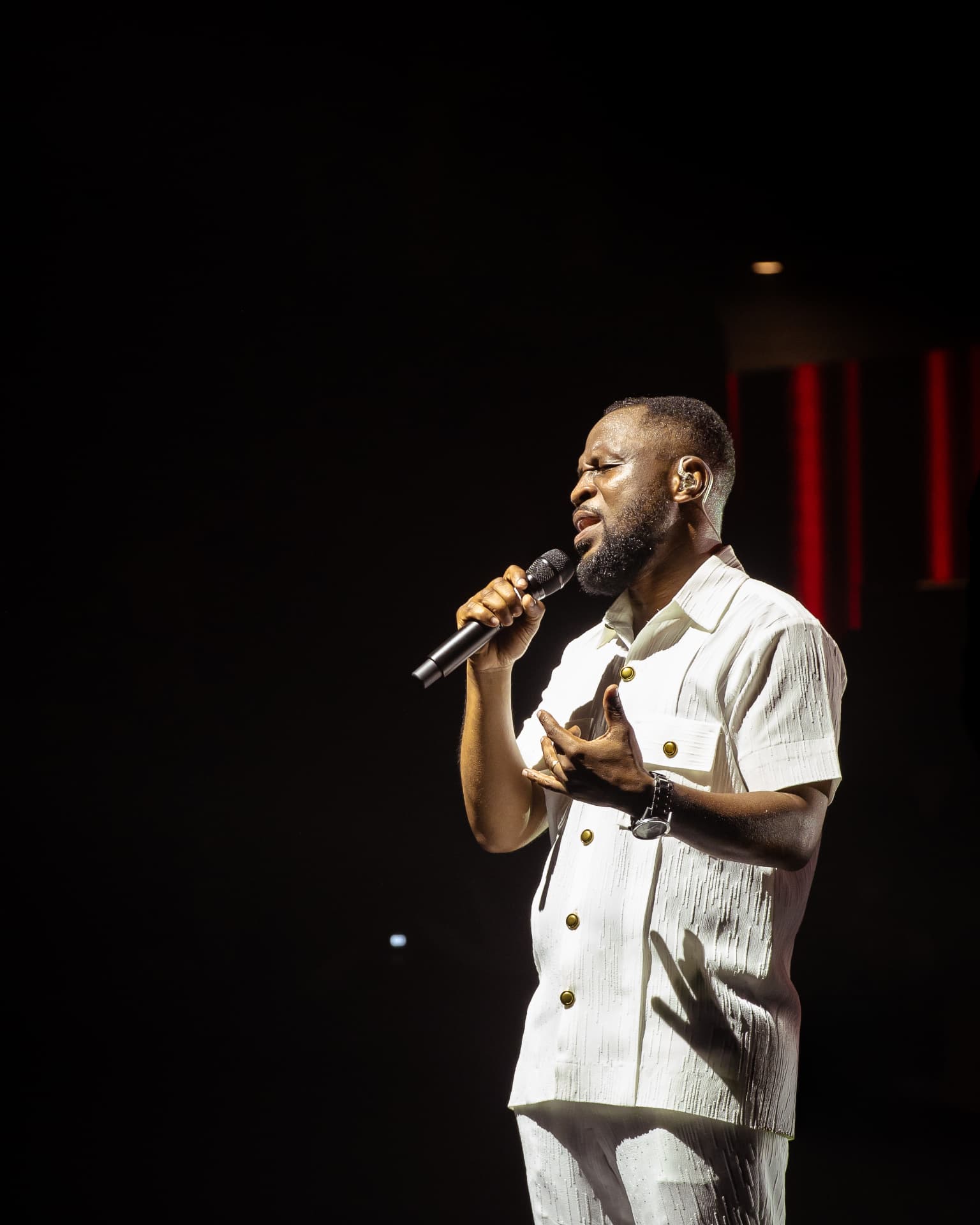 Pastor Edwin Dadson singing in white with a microphone during live worship